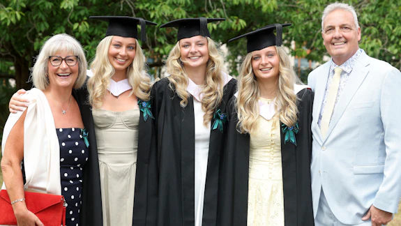 A man and woman pose for a photo with three female graduates in their hats and gowns.