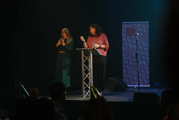 A woman is delivering a speech on stage alongside a BSL interpreter