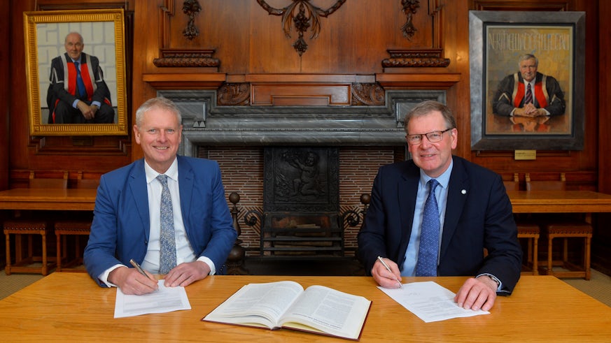 Professor Colin Riordan and Malcolm Harrison of CIPS group sat at a table in Cardiff University signing a memorandum of understanding