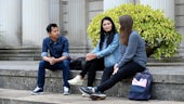 Group of three students sat outside a university building