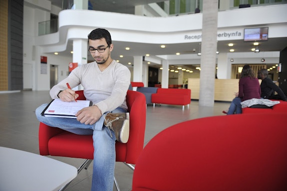 Male student hands holding pen, completing postgraduate application form
