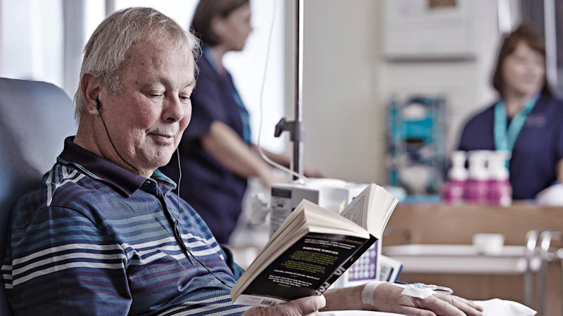 Man in a hospital reading a book, hooked up to a medical machine.