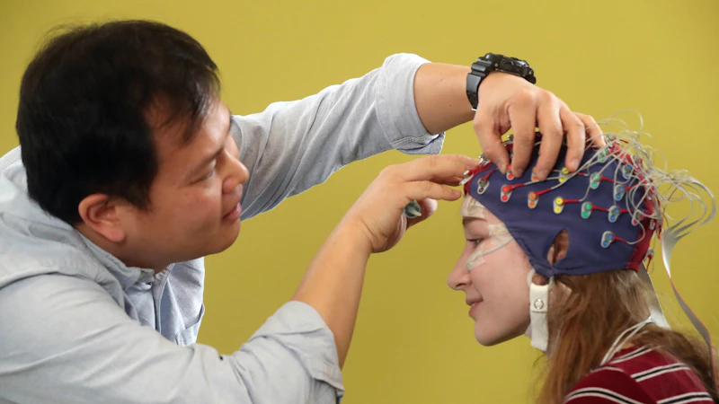 a male researcher attached electrodes to a female participants head to prepare for a brain imaging study