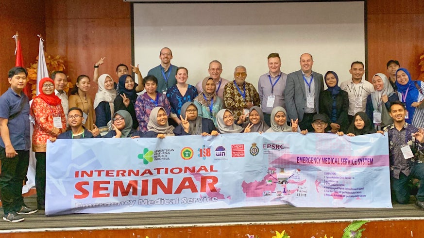 Group of Indonesian and British researcher standing in front of a banner showing, Emergency Sevices International Seminar.