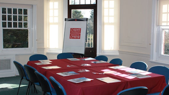 Room with table and chairs, laid with red tablecloth, papers on table, a table at front of room and flipchart.