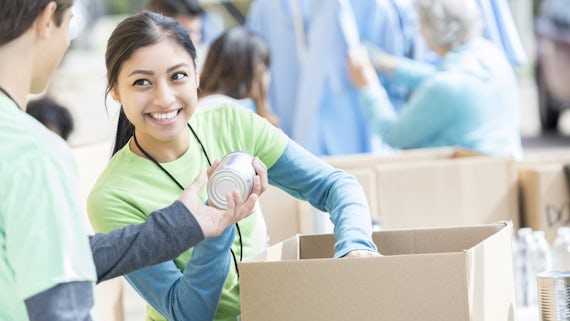 Male and female teenage food bank volunteers sort canned food items in cardboard boxes