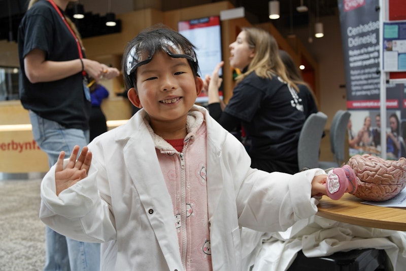 A child wearing a lab coat and safety goggles investigates brain model.