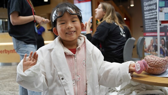 A child wearing a lab coat and safety goggles investigates brain model.