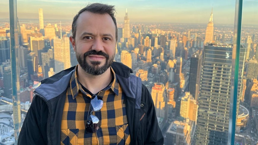 A portrait of Dr Giulio Fabbian on a skyscraper viewing point with the skyline of a metropolitan city behind him
