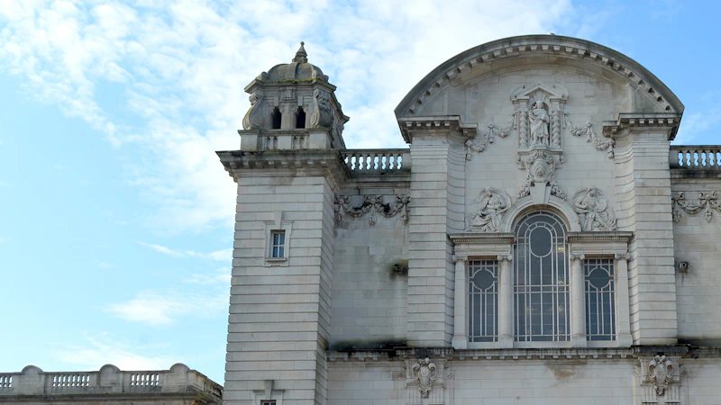 A cropped image of the top of a white stone building, the sky is blue