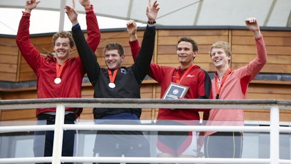 Four members of Cardiff University rowing quad smiling and waving, wearing their medals