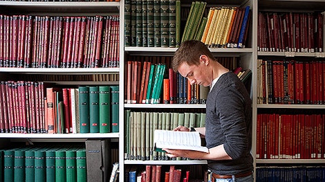 Male student reading in front of a wall of books