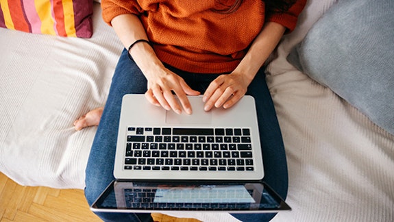 Female student sat on bed working on laptop