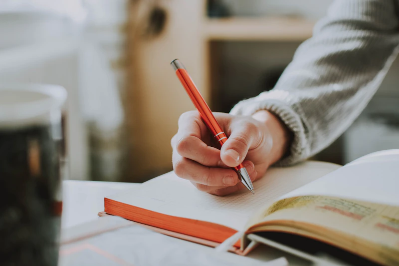 A person with a pen writes on a notebook