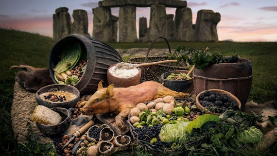A suckling pig and other food laid out in front of Stonehenge.