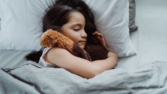 Child asleep in bed holding a teddy bear