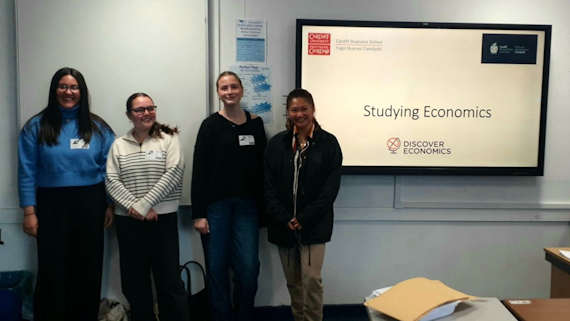4 students stood at the front of a class smiling, about to present a Study Economics workshop