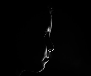 Photo of child's face in profile in darkness. Child is looking towards the right of the image, towards a source of a light not shown.