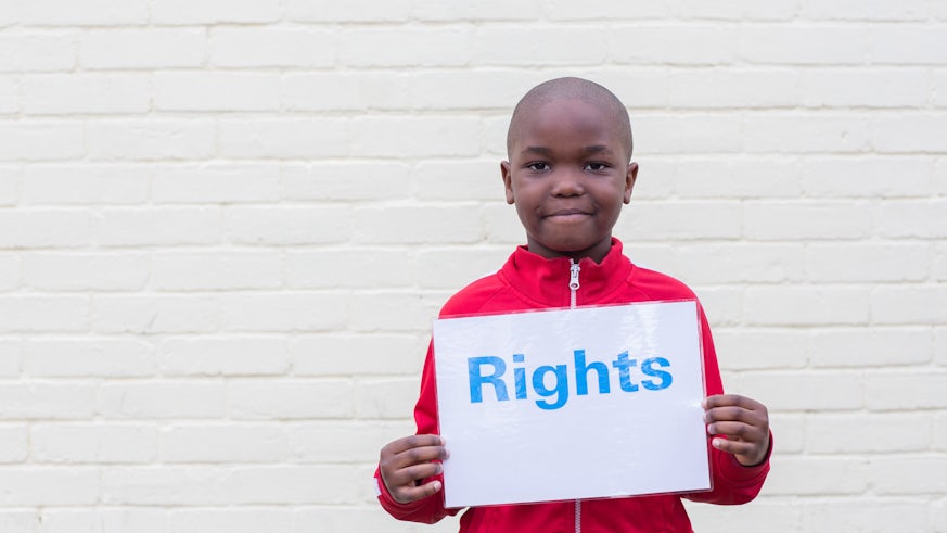a boy holds up a sign saying 'rights' to the camera