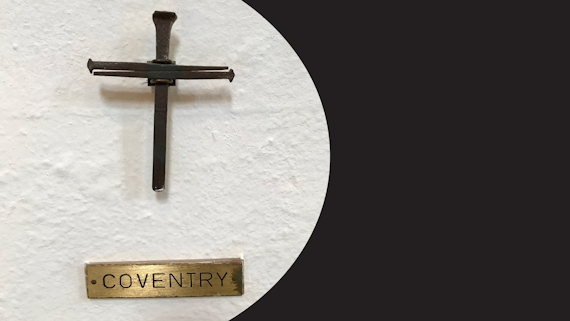 A brown cross on a white wall with a plaque entitled 'Coventry' underneath