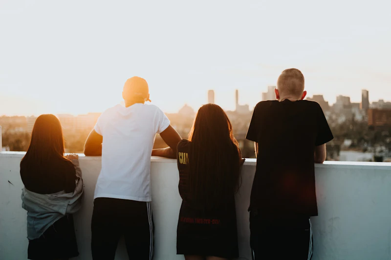 Image shows four young people, standing in front of a white wall, looking away from the camera.