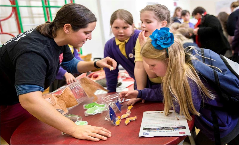 A female scientist demonstrating a biomagnification game to three school children