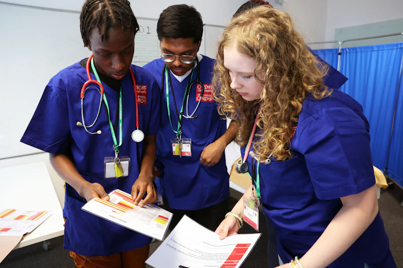 Participants wearing medical scrubs looking at printed patient information during a clinical skills activity.