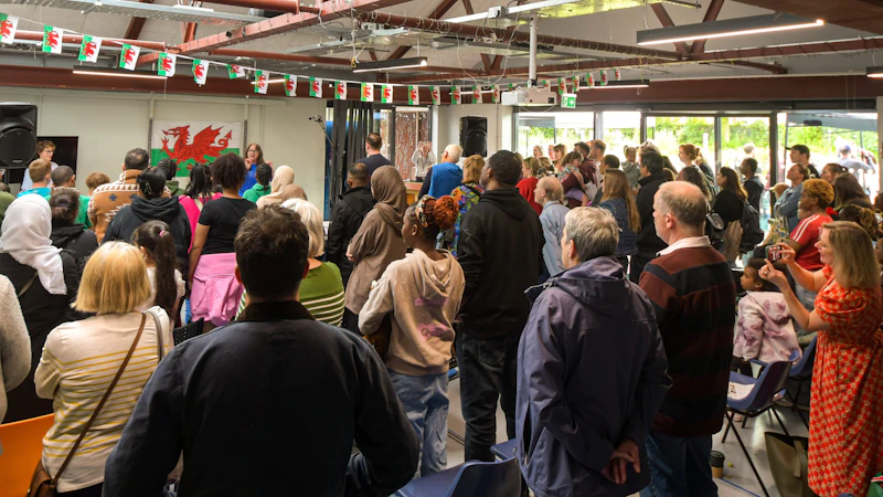 A crowd of people are gathered in a hall. They are looking at a stage where the Welsh flag is displayed. 