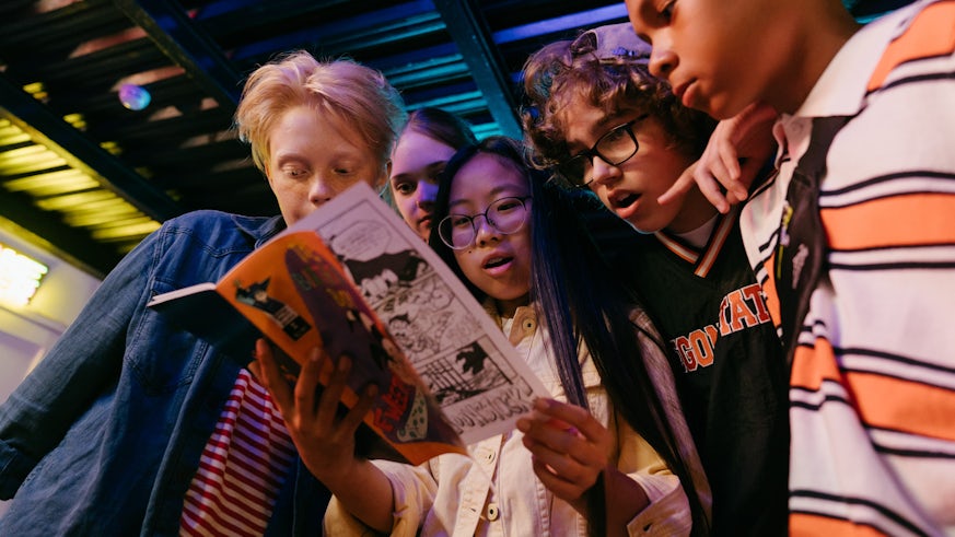 A diverse group of children hold and read a magazine together