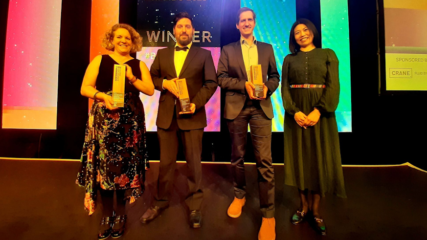The Welsh School of Architecture’s Low Carbon Built Environment (LCBE) team holding three trophies on stage at the National CIBSE Performance Awards 2023.
