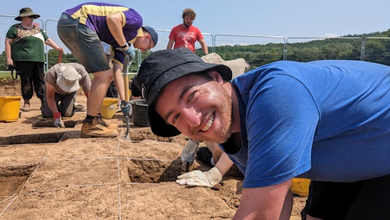 Mid shot man smiling at camera with archaeological dig in the background
