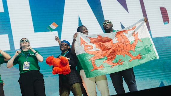 Students are photographed on the stage at a competition. One is holding a Welsh flag.