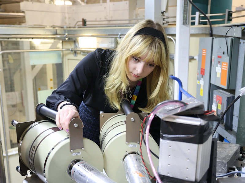 A woman operates a physics research instrument in a laboratory.