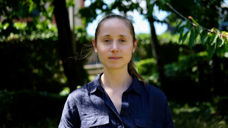  A photograph of a young woman in a sunlit garden surrounded by trees.
