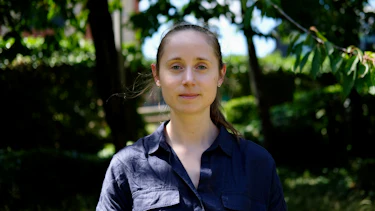 A photograph of a young woman in a sunlit garden surrounded by trees.