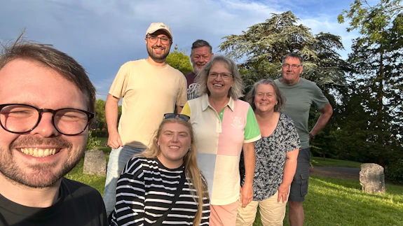 A photo of seven people smiling at the camera on a sunny day.