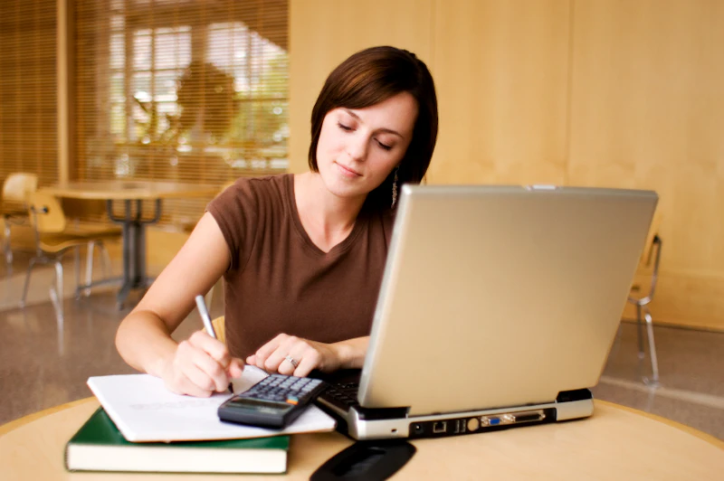 Woman with brown hair sitting at a desk and writing on a piece of paper. 