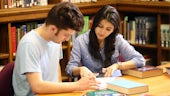 Male and female student working at table in library