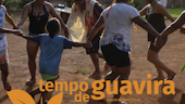 People hold hands dancing in a circle with the words Tempo de Guavira in orange letters