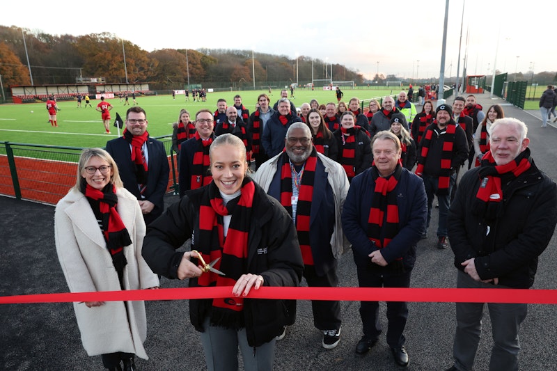 Young woman cuts ribbon with crowd of people and playing fields behind her