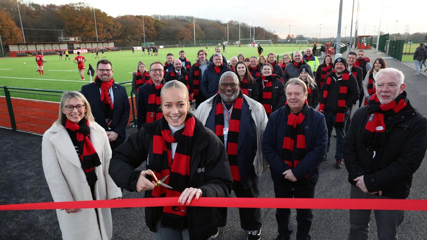 Young woman cuts ribbon with crowd of people and playing fields behind her