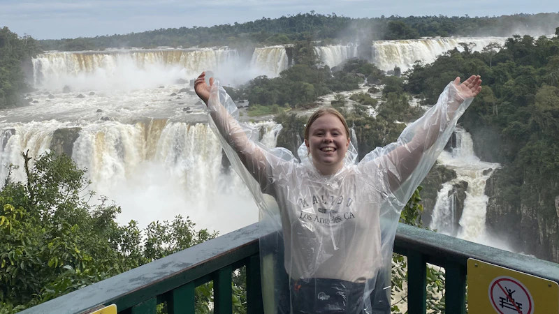 A photo of a female smiling at the camera with a waterfall in the background.