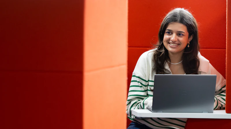 Smiling female student using a laptop in a booth.