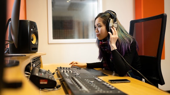 A female student listening at a sound mixing desk