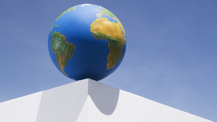 A replica globe of planet Earth balances on the corner of a white pl