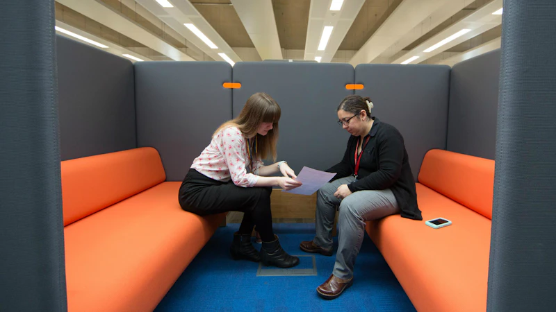 Two women sitting and facing each other and looking over documents.