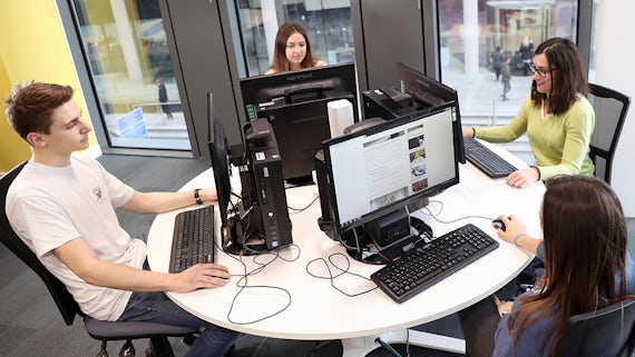 Four students sit around a table, each is working at a computer