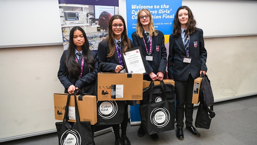 Four schoolgirls pose for photograph holding laptops and a certificate
