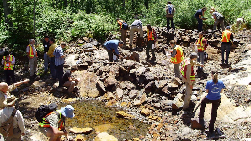 Lots of people wearing high-visibility vests examining an exploration trench in Canada