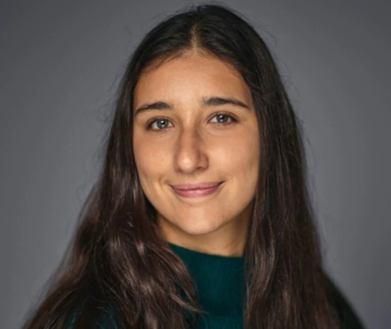 A profile style picture of a young woman with long brown hair who is wearing a green jumper and smiling